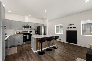 Una cocina moderna con armarios grises, un refrigerador de acero inoxidable, un microondas y una isla central con taburetes de bar.
