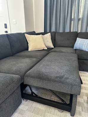 A sectional sofa with a dark fabric, two pillows, and a black metal frame. - New Cozy Modern Cottage with Hot Tub & Fire Pit! (Ponderay)