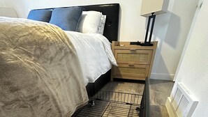A bedroom with a bed, a nightstand, a lamp, and a radiator. - New Cozy Modern Cottage with Hot Tub & Fire Pit! (Ponderay)