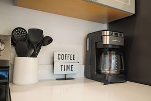 A kitchen counter with a coffee maker, a sign that reads "COFFEE TIME," and a container holding kitchen utensils.