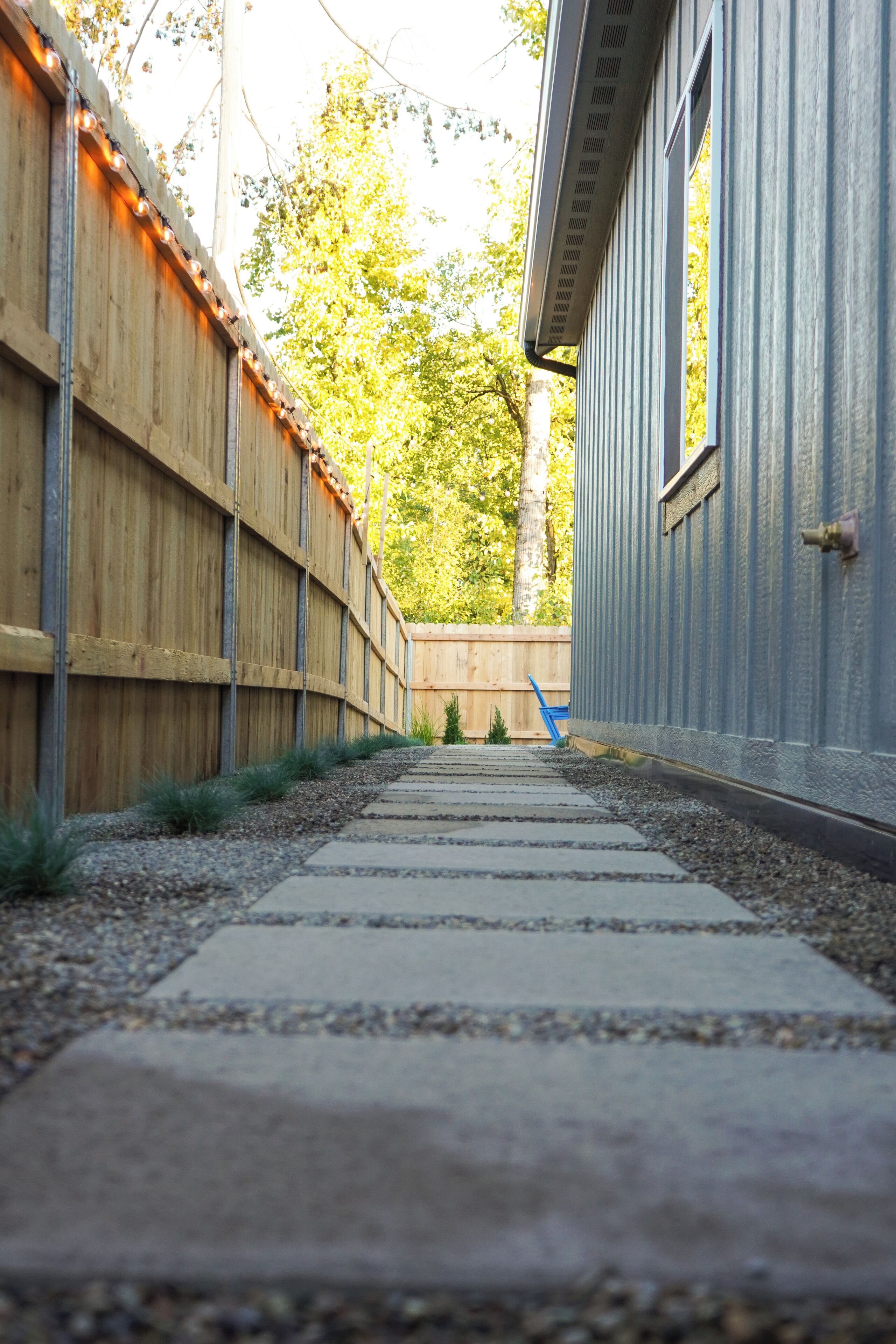 A pathway leading to a building with a wooden fence on one side and a metal siding on the other.
