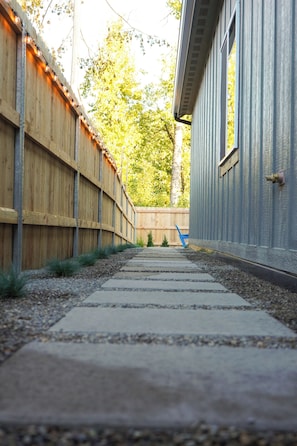 A pathway leading to a building with a wooden fence on one side and a metal siding on the other.