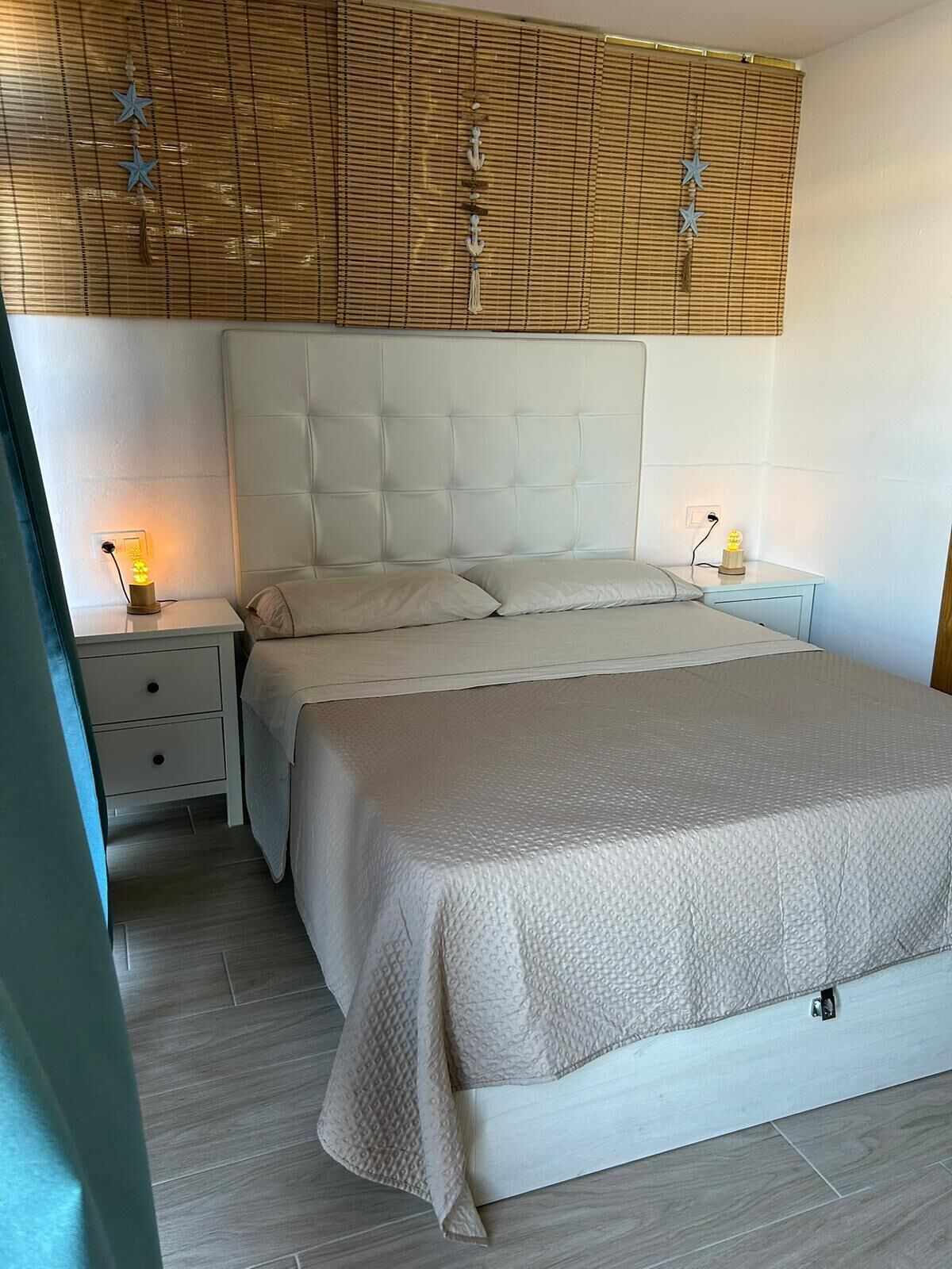 Une chambre à coucher avec un grand lit, deux tables de chevet, une lampe fixée au mur et une tête de lit à motifs.