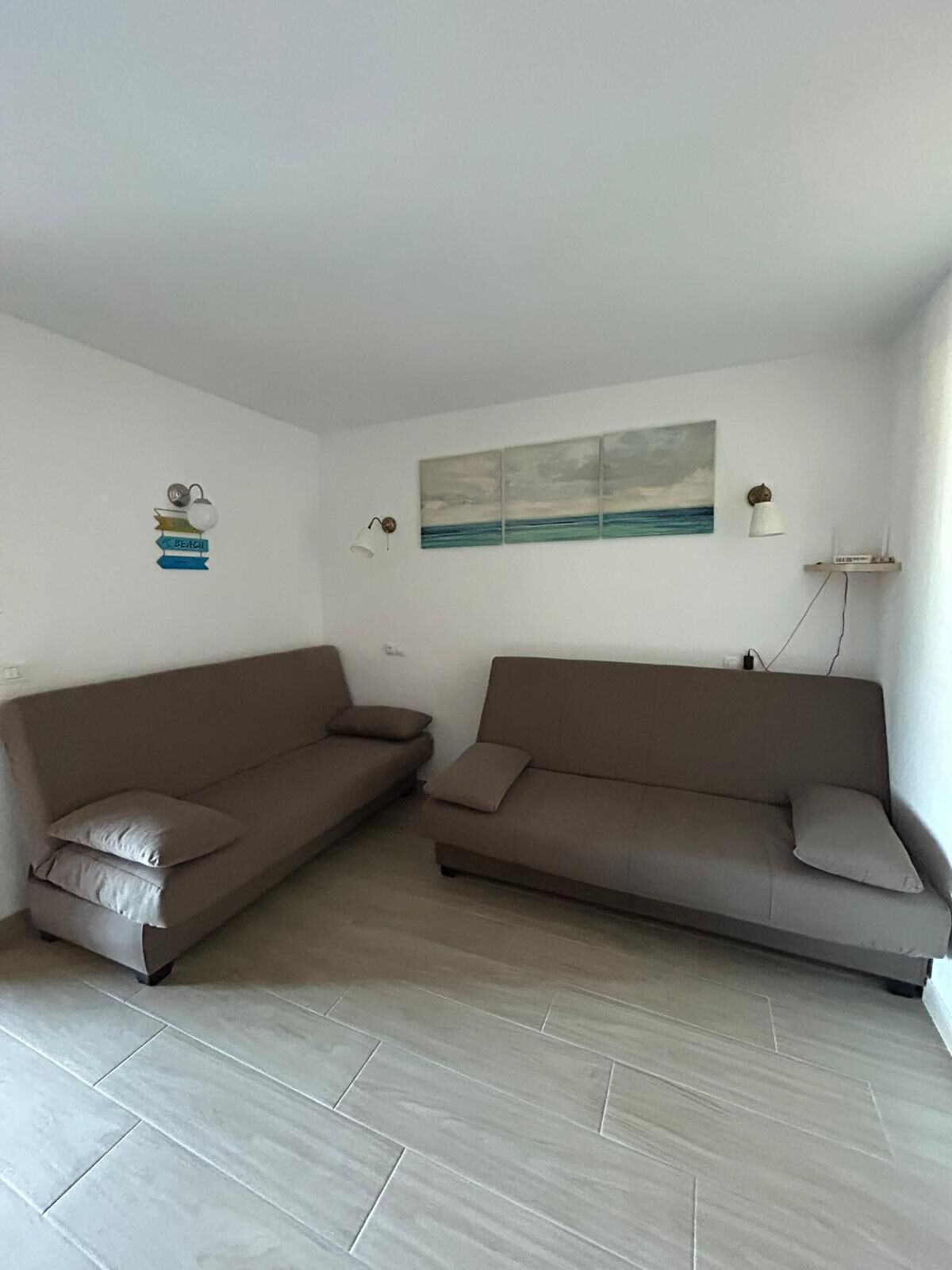 Een woonkamer met twee banken, een aan de muur hangend schilderij en een klein kastje met kaarsen.