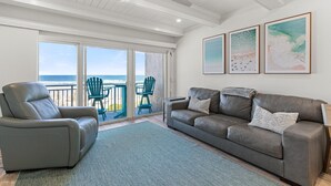 A living room with a gray leather sofa, a gray leather chair, and a green rug. There are three framed artworks on the wall and a ceiling fan.