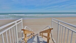 A wooden staircase leading to a beach with white railings.