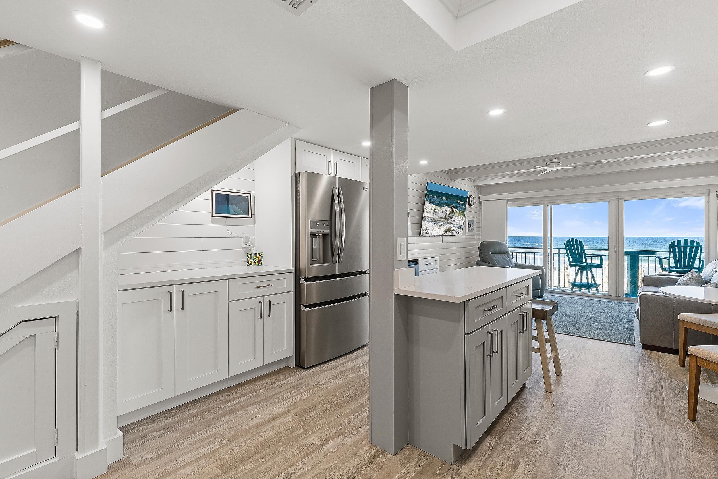 A modern kitchen with white cabinetry, a stainless steel refrigerator, and a dining area with a view of the ocean.