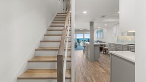 A modern kitchen with grey cabinets, a wooden staircase, and a view to the outside.