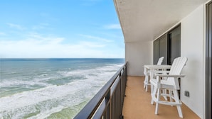 Een balkon met witte stoelen en een tafel, met uitzicht op de oceaan.
