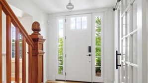 Un pasillo con una escalera de madera, una puerta blanca con paneles de vidrio y una lámpara en el techo.