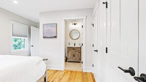 Un dormitorio con cama, ventana, puerta que da a un baño y vista al exterior.