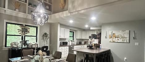 A modern kitchen with white cabinets, a dining area with a dark wood table, and a chandelier.