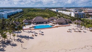 Un complexe hôtelier doté d’une grande piscine, d’une plage et de bâtiments à toits de chaume.
