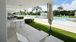 Une terrasse extérieure moderne, avec des meubles blancs, une piscine et des palmiers.