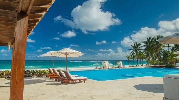 Un espace piscine avec des chaises longues et des parasols, une pergola en bois et une vue sur l’océan.