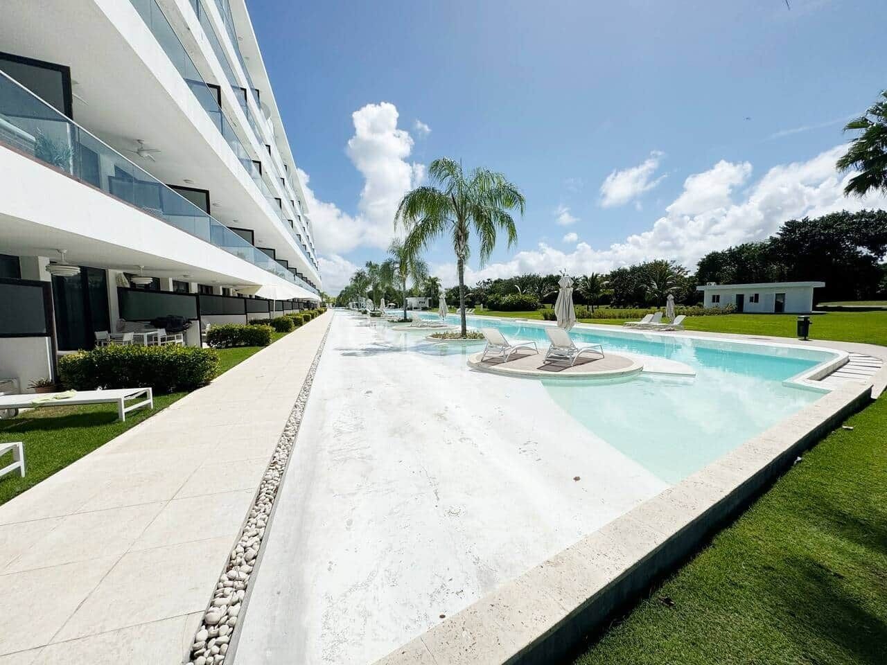 Un hotel moderno con piscina, sillones de descanso y un césped bien cuidado.