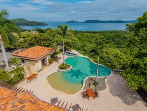 A resort with a swimming pool, outdoor seating, and a view of the sea.