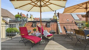 A rooftop terrace with outdoor seating, including red and striped chairs, and a large beige umbrella. - Cozy vacation apartment "Inselglück" - roof terrace, lake view, central (Lindau)