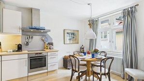 A modern kitchen with white cabinets, a built-in oven, and a dining area with a wooden table and chairs. - Cozy vacation apartment "Inselglück" - roof terrace, lake view, central (Lindau)