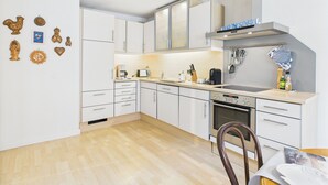 A modern kitchen with white cabinets, a built-in oven, and a stainless steel range hood. - Cozy vacation apartment "Inselglück" - roof terrace, lake view, central (Lindau)