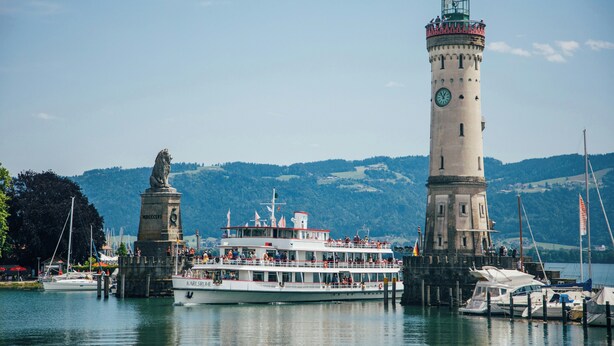A large white boat docked at a harbor with a prominent lighthouse and a statue in the background. - Cozy vacation apartment "Inselglück" - roof terrace, lake view, central (Lindau)