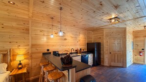 A wooden cabin interior with a kitchen, dining area, and bar stools. - Grace - Big Moose Lakeside (Eagle Bay)