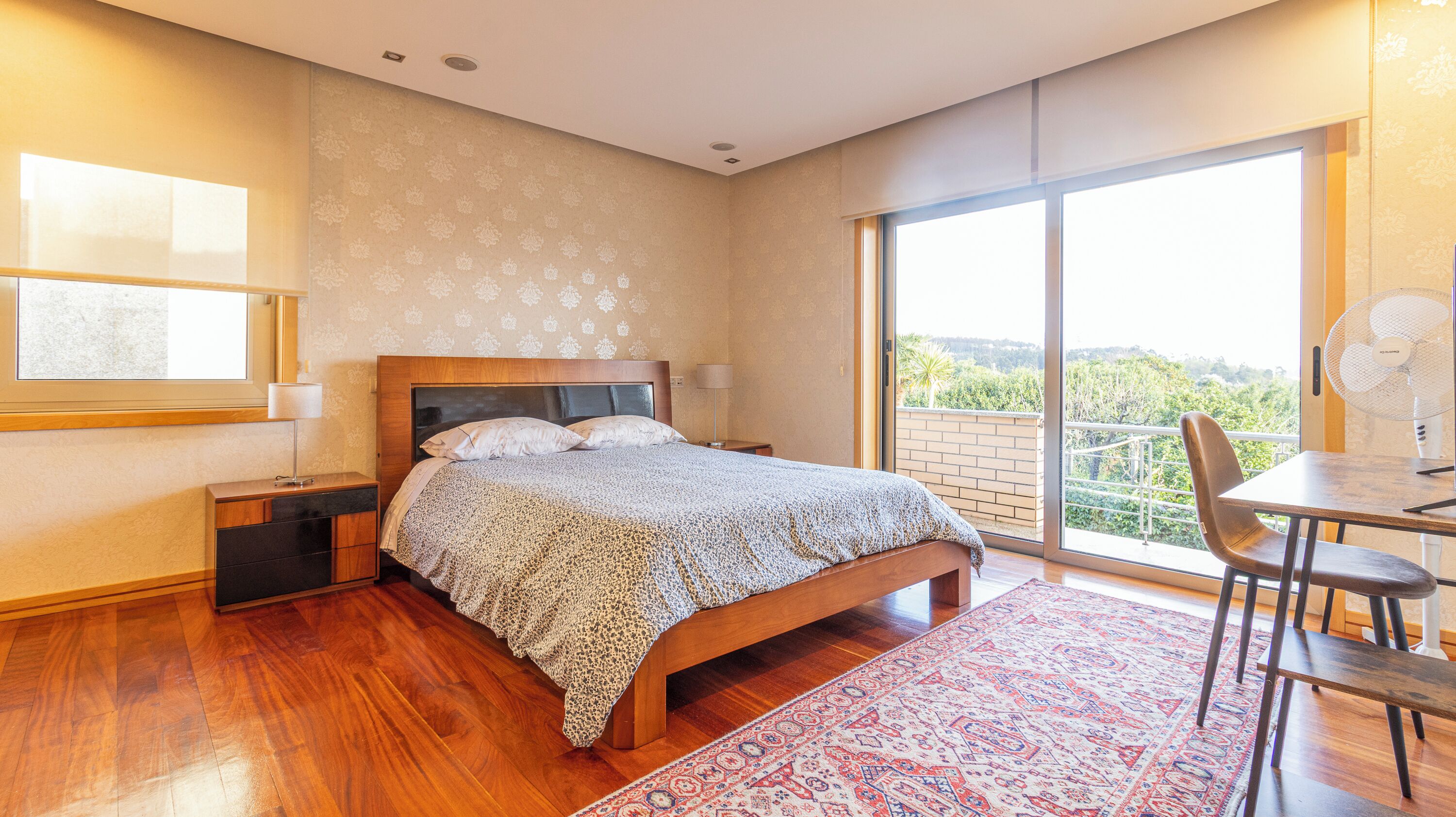 Une chambre à coucher avec un grand lit, une table de chevet, un bureau avec une chaise, une fenêtre et un balcon.