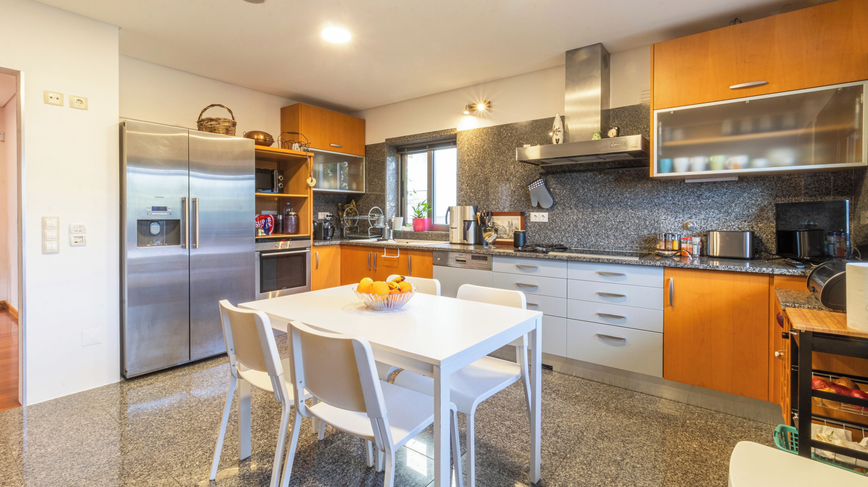 A modern kitchen with stainless steel appliances, a granite countertop, and a dining area with white chairs.