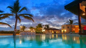 A swimming pool with palm trees and a building with a roof.
