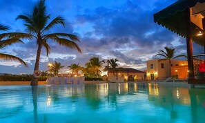 Una piscina con palmeras, un edificio con techo y un cielo al atardecer.