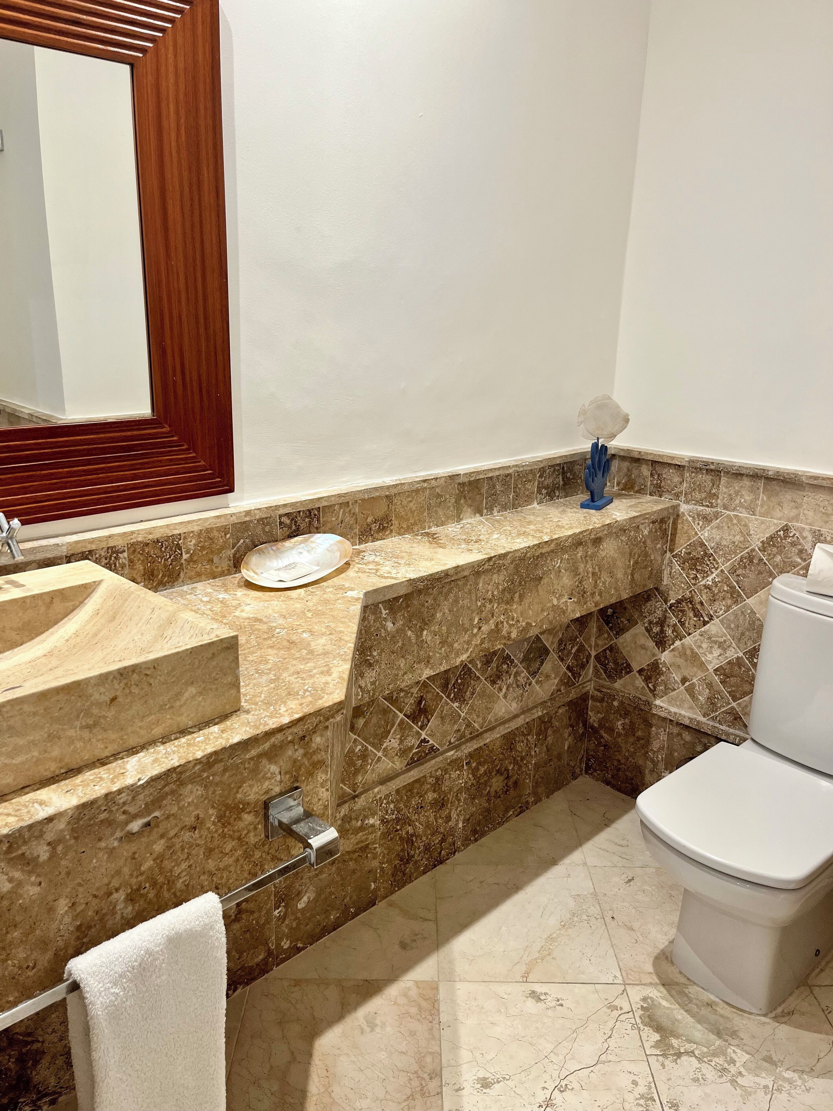 Un baño con lavamanos de mármol, inodoro y espejo con marco de madera.