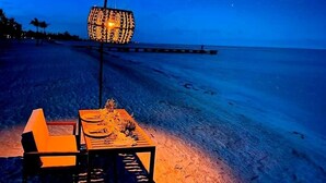 A beach scene with a table and chairs under a starry sky.