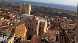 A coastal cityscape with a mix of traditional and modern buildings, a prominent tower, and a view of the sea.