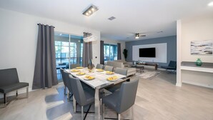 Ein modernes Wohnzimmer mit Essbereich, großen Fenstern und einem an der Wand befestigten Flachbildfernseher.