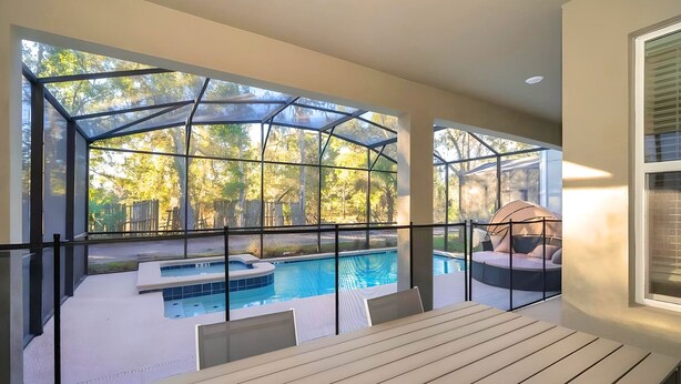 Ein moderner Poolbereich im Freien mit Glasveranda, Whirlpool und einer Sitzecke mit Kissen.