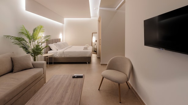 Una habitación de hotel moderna con una cama, un sofá, una silla, una mesita de café y un televisor montado en la pared.