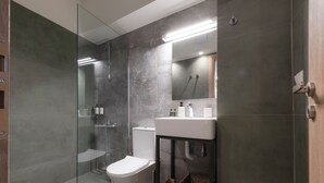 Un baño moderno con cabina de ducha de vidrio, inodoro blanco y tocador con espejo.