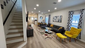 A spacious living area with a staircase, a dining area, and a kitchen in the background.