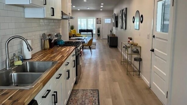 A modern kitchen with white cabinets, a wooden countertop, and a stainless steel sink.