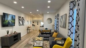 A modern living room with a sofa, yellow chairs, a TV, and artwork on the walls.