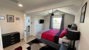 A bedroom with a bed, a desk, a chair, a TV, and a window.