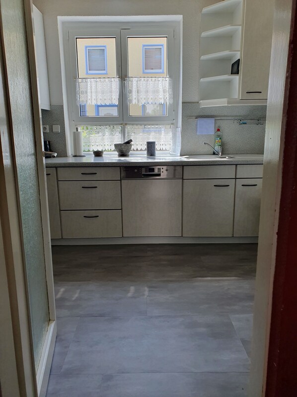 Una cocina con lavavajillas, una ventana con cortinas de encaje y un lavabo con dispensador de jabón.
