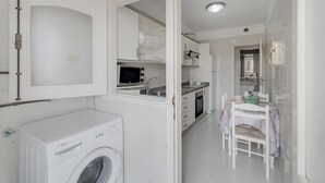 Cocina compacta con microondas, lavaplatos y horno, comedor con mesa y sillas, y lavadora.