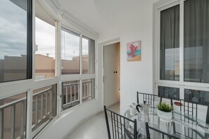 A balcony with a glass table, chairs, a potted plant, and a painting on the wall.