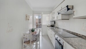 Una cocina estrecha con armarios blancos, encimera de granito y comedor con mesa dispuesta para dos.