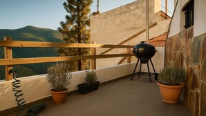 A balcony with a wooden railing, a barbecue grill, and potted plants. - Casa Cueva Barranco Hondo (Gáldar)