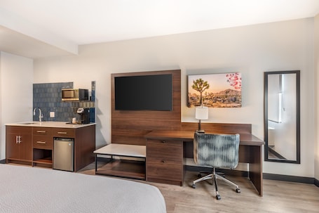 A hotel room with a bed, a desk with a chair, a TV mounted on the wall, a microwave, and a sink with a dishwasher.. Best Western Plus Rialto