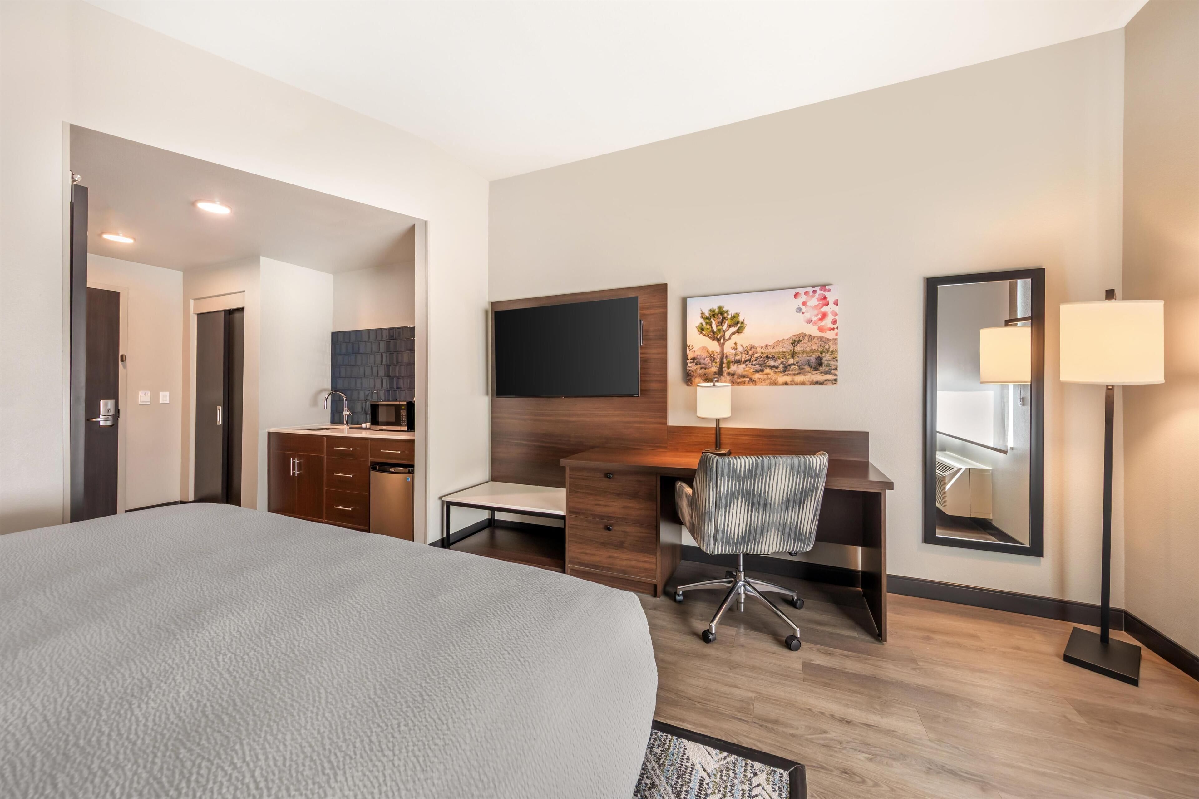 A hotel room with a bed, a desk with a chair, a flat-screen TV, a mirror, and a lamp.