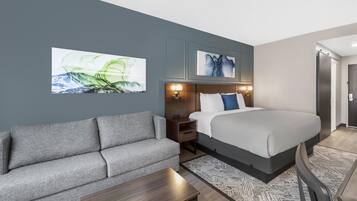 A modern hotel room with a bed, a sofa, a nightstand, and artwork on the walls.