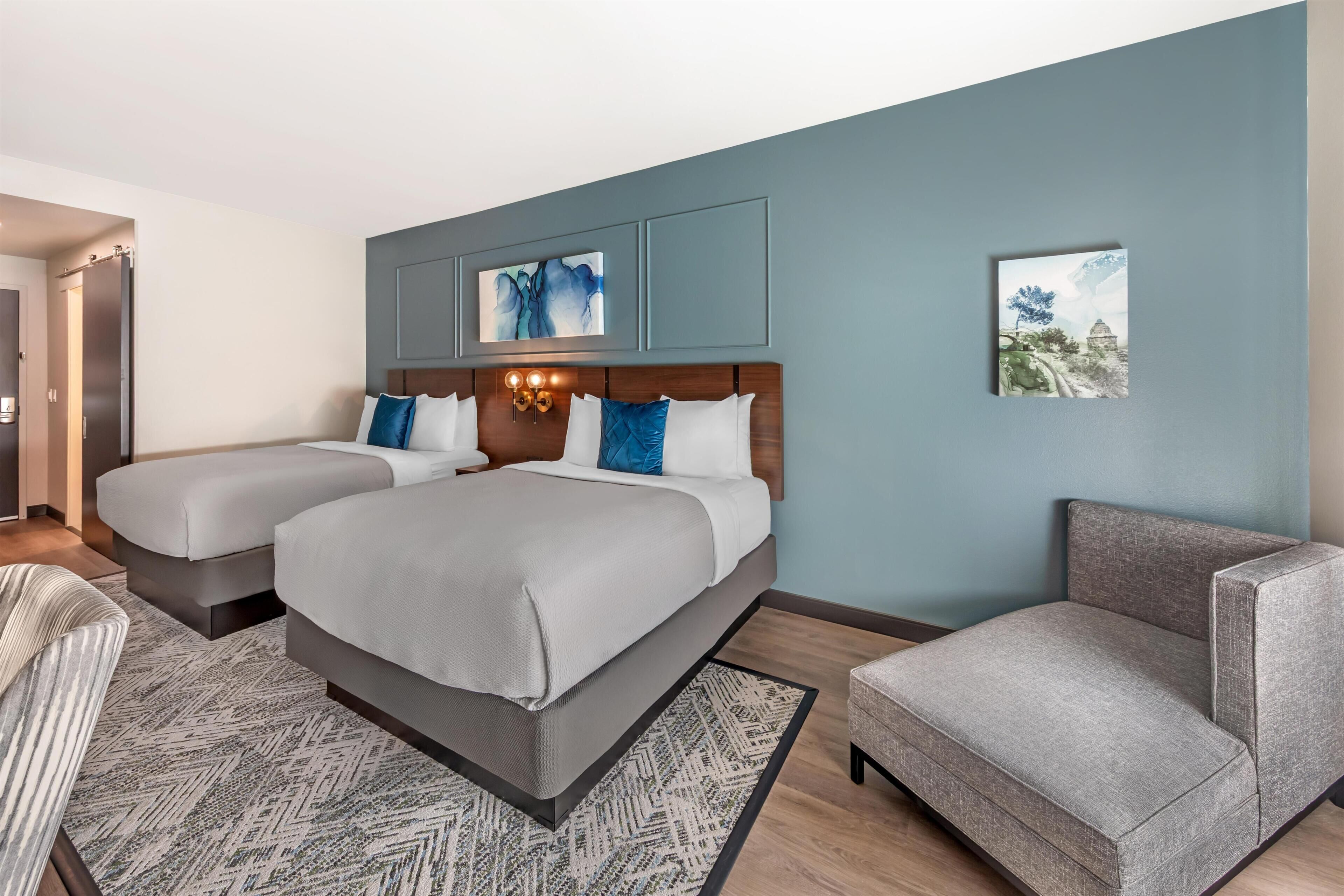 Una habitación de hotel con una cama grande, dos mesitas de noche, una silla y obras de arte en las paredes.
